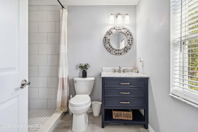 bathroom with toilet, plenty of natural light, vanity, and a tile shower