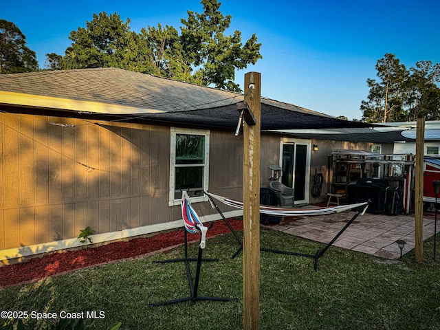 back of property featuring a yard, a shingled roof, and a patio area