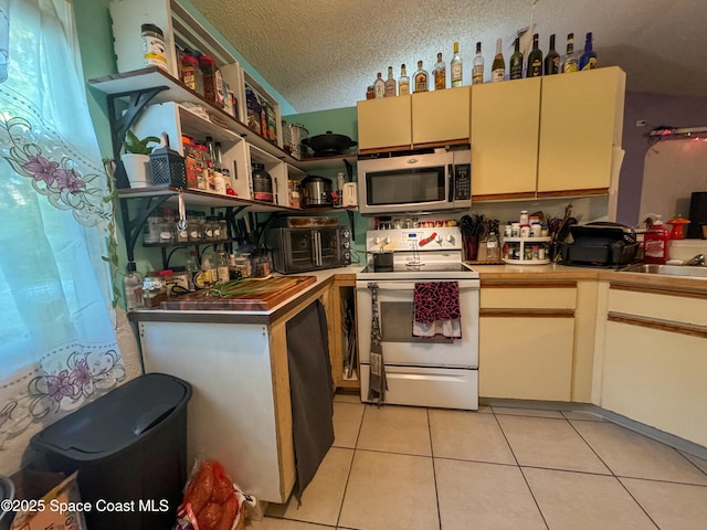 kitchen featuring light tile patterned floors, cream cabinetry, a textured ceiling, stainless steel microwave, and white electric range