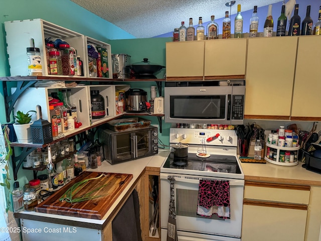 kitchen with stainless steel microwave, white electric stove, a textured ceiling, and cream cabinetry