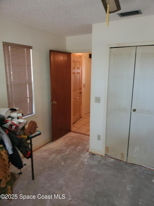 unfurnished bedroom with visible vents, unfinished concrete flooring, a textured ceiling, and a closet