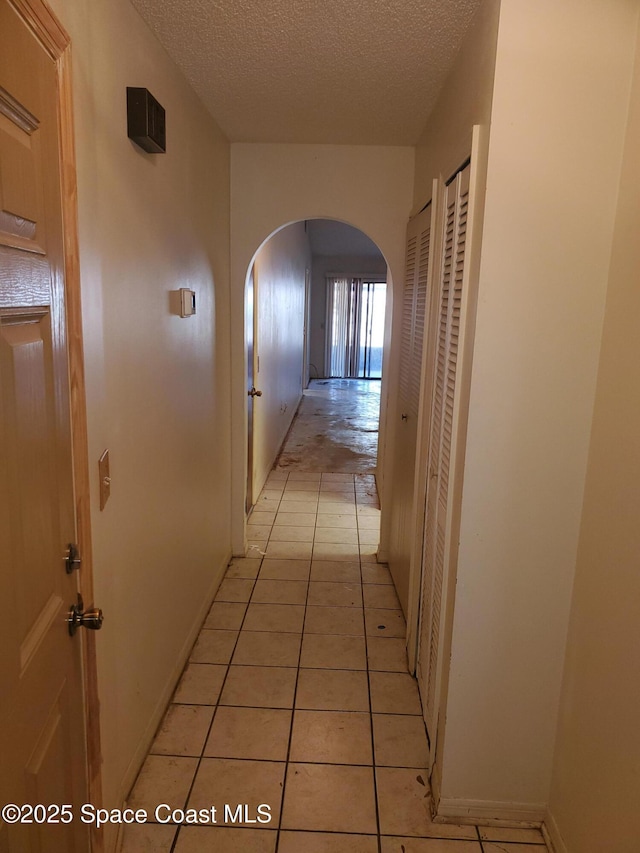 hallway with light tile patterned floors, baseboards, arched walkways, and a textured ceiling