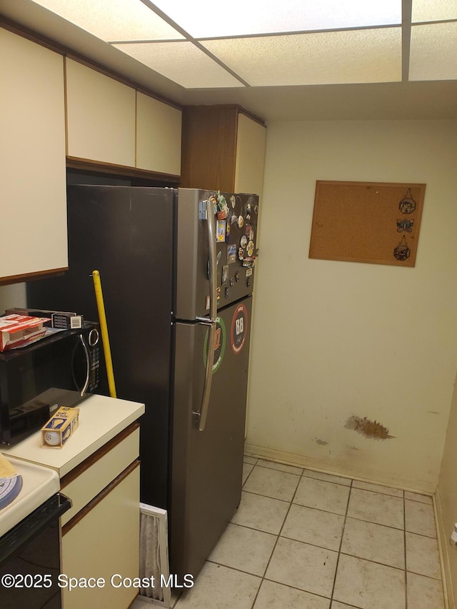 kitchen featuring light tile patterned floors, cream cabinetry, light countertops, and black microwave