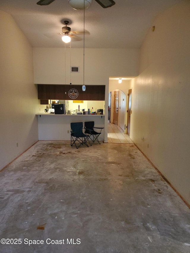 kitchen with arched walkways, unfinished concrete floors, a high ceiling, and ceiling fan