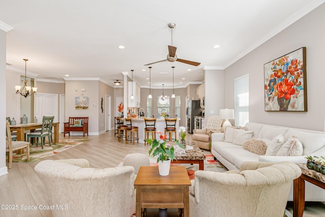 living area featuring crown molding, light wood finished floors, ceiling fan with notable chandelier, and a wealth of natural light