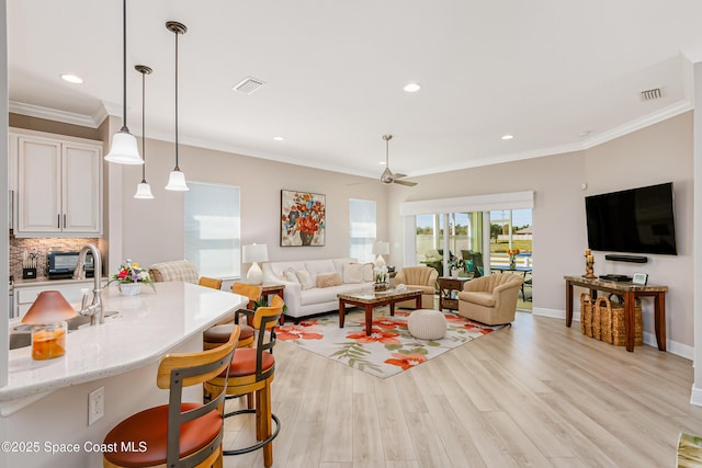 living area featuring light wood finished floors, visible vents, crown molding, and baseboards