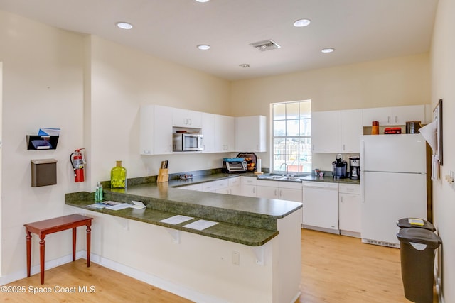 kitchen with dark countertops, visible vents, a peninsula, white appliances, and a sink