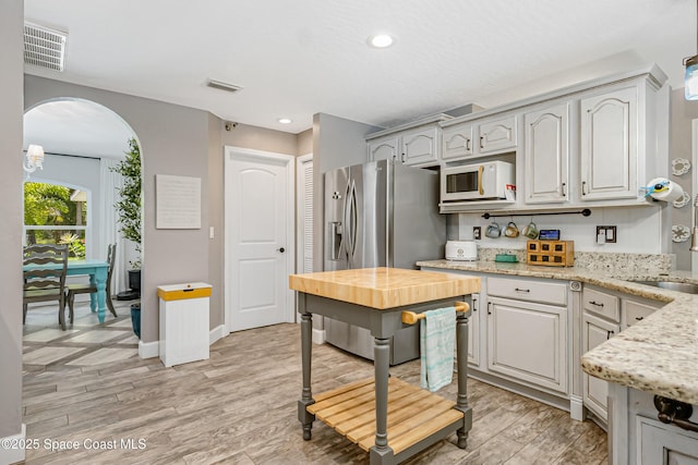 kitchen featuring white microwave, visible vents, light wood-style flooring, stainless steel refrigerator with ice dispenser, and arched walkways