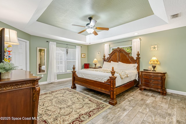 bedroom with visible vents, a raised ceiling, baseboards, and light wood finished floors