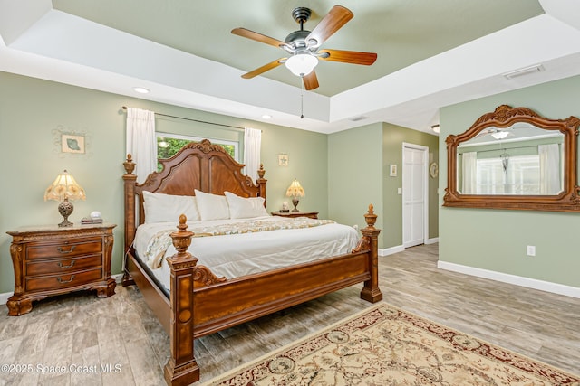 bedroom featuring wood finished floors, baseboards, visible vents, ceiling fan, and a raised ceiling