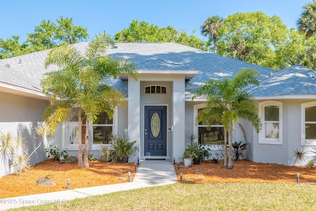 view of exterior entry with stucco siding and roof with shingles