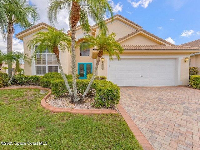 mediterranean / spanish house with a tile roof, decorative driveway, an attached garage, and stucco siding