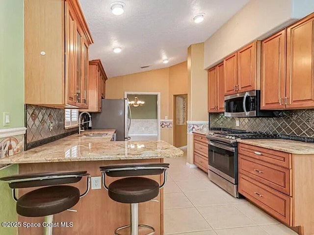 kitchen featuring appliances with stainless steel finishes, a breakfast bar, a peninsula, and light stone countertops