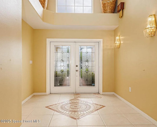 tiled entrance foyer featuring a wealth of natural light, french doors, a high ceiling, and baseboards