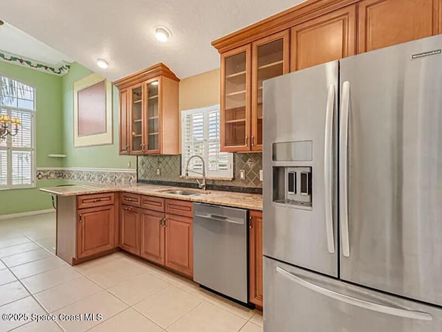 kitchen featuring light tile patterned floors, decorative backsplash, appliances with stainless steel finishes, a peninsula, and brown cabinetry