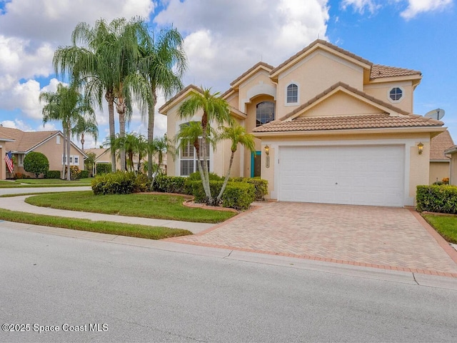 mediterranean / spanish-style home with stucco siding, decorative driveway, a front yard, a garage, and a tiled roof