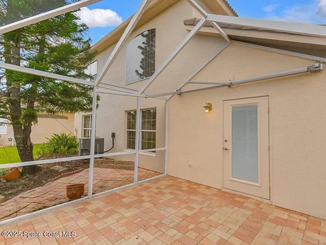 rear view of property featuring glass enclosure, a patio, cooling unit, and stucco siding