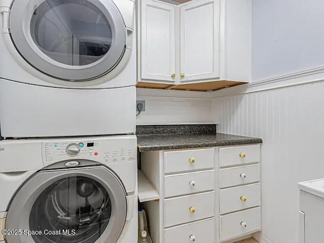 clothes washing area featuring wainscoting, cabinet space, and stacked washing maching and dryer