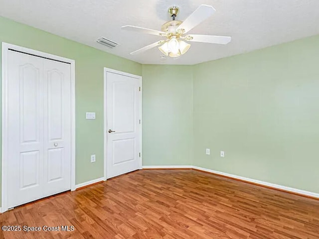 unfurnished bedroom featuring visible vents, wood finished floors, a closet, baseboards, and ceiling fan