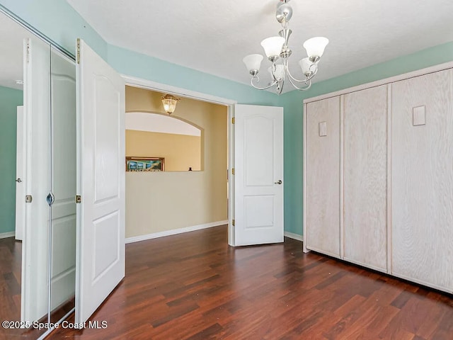 unfurnished bedroom with a closet, an inviting chandelier, baseboards, and wood finished floors