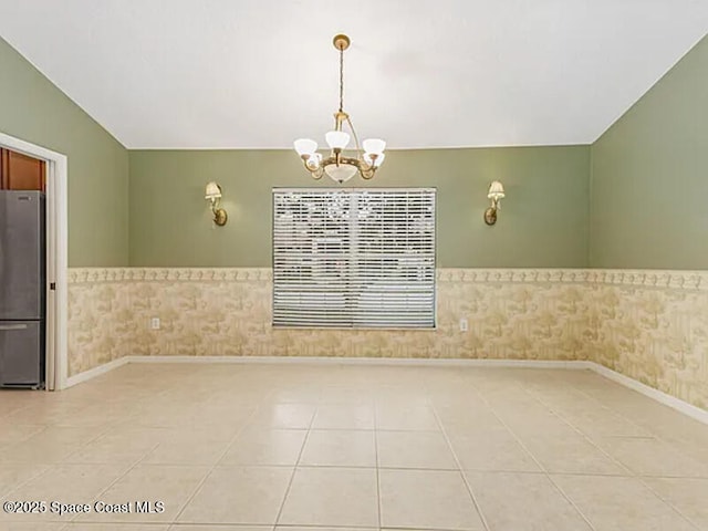 spare room with lofted ceiling, an inviting chandelier, wainscoting, tile patterned flooring, and baseboards