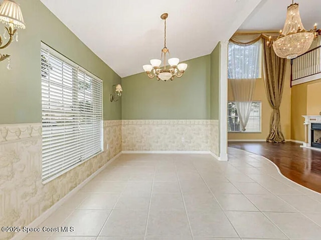 tiled empty room featuring a wainscoted wall, a notable chandelier, a fireplace, wallpapered walls, and baseboards