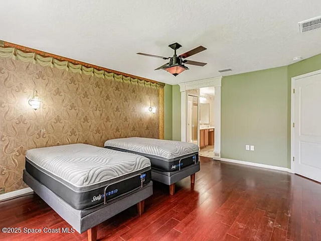 bedroom featuring visible vents, ensuite bathroom, wood finished floors, wallpapered walls, and baseboards