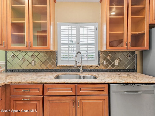 kitchen featuring dishwasher, light stone counters, glass insert cabinets, and a sink