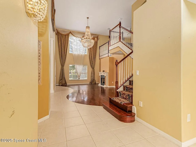 entrance foyer featuring baseboards, stairway, a fireplace, tile patterned floors, and a notable chandelier