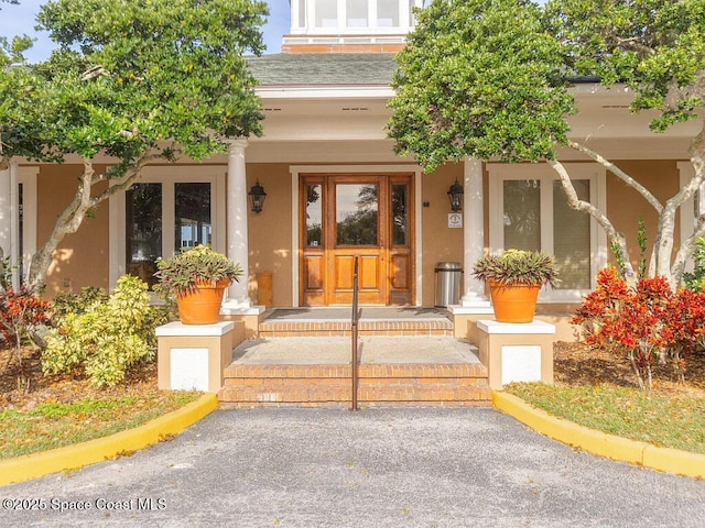 doorway to property featuring stucco siding, a porch, and roof with shingles