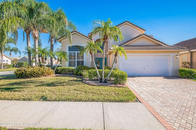 view of front of home featuring stucco siding, decorative driveway, a front lawn, and a tiled roof