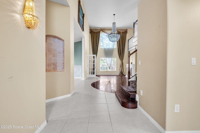 hall with baseboards, a chandelier, stairs, a high ceiling, and tile patterned floors