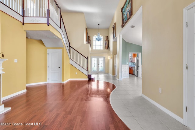 entrance foyer with wood finished floors, french doors, baseboards, a towering ceiling, and stairs