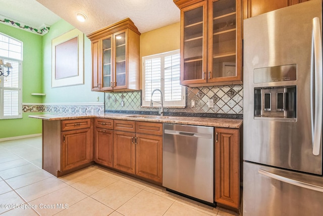 kitchen featuring brown cabinetry, light tile patterned flooring, a sink, stainless steel appliances, and glass insert cabinets