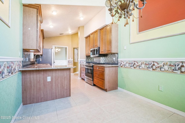 kitchen featuring light stone countertops, light tile patterned floors, brown cabinets, appliances with stainless steel finishes, and a notable chandelier