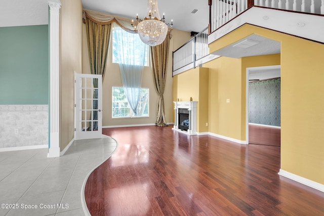 unfurnished living room featuring a fireplace with raised hearth, wood finished floors, an inviting chandelier, baseboards, and a towering ceiling
