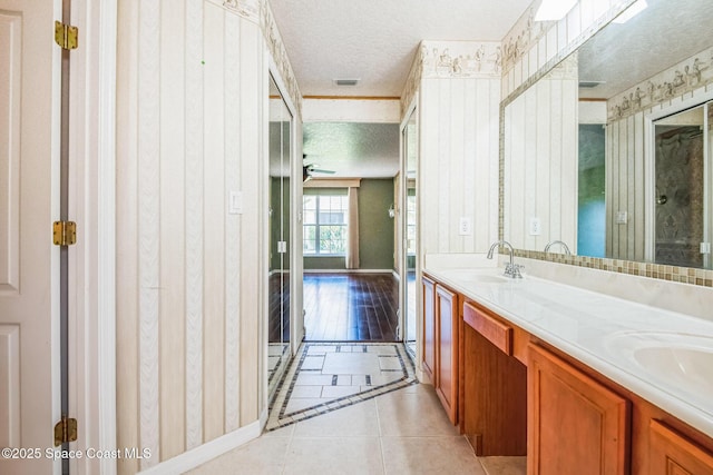 full bath featuring tile patterned flooring, visible vents, double vanity, a textured ceiling, and a sink