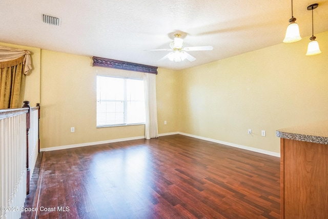 spare room featuring visible vents, baseboards, ceiling fan, dark wood finished floors, and a textured ceiling