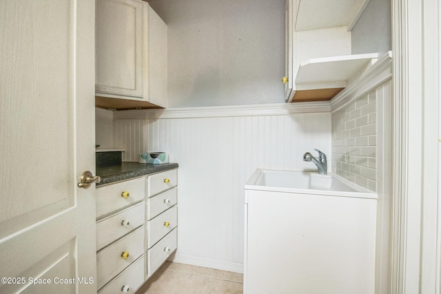 laundry room with a sink, light tile patterned flooring, and wainscoting