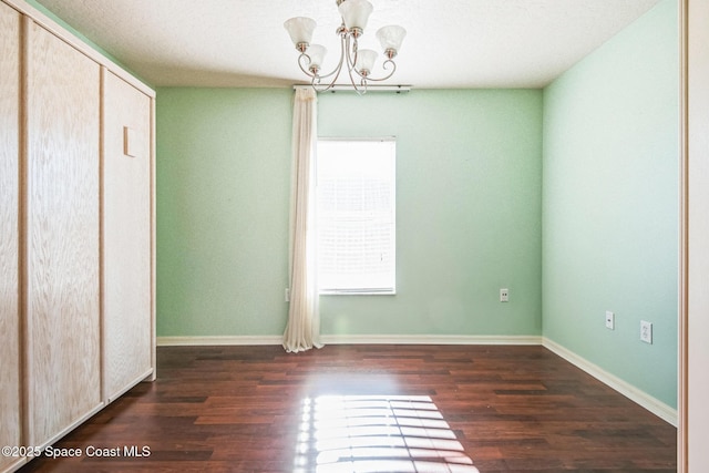 unfurnished bedroom featuring an inviting chandelier, wood finished floors, baseboards, and a closet