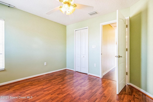 unfurnished bedroom featuring wood finished floors, visible vents, baseboards, ceiling fan, and a closet
