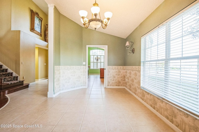 empty room with light tile patterned floors, a wainscoted wall, stairs, vaulted ceiling, and a chandelier