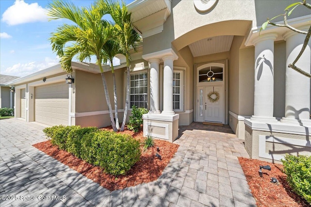 view of exterior entry featuring stucco siding, decorative driveway, and an attached garage