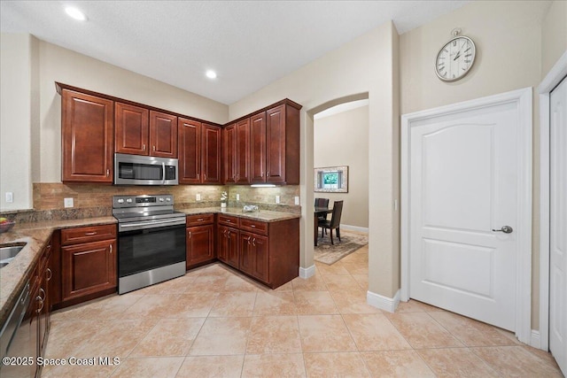 kitchen featuring light stone counters, light tile patterned floors, arched walkways, stainless steel appliances, and tasteful backsplash