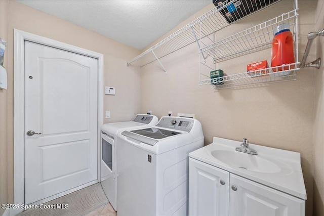 washroom with cabinet space, washing machine and dryer, a textured ceiling, and a sink