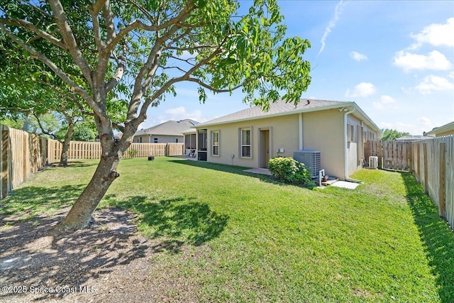 rear view of house with stucco siding, a yard, central AC unit, and a fenced backyard