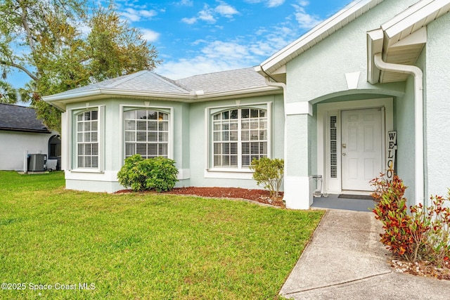 property entrance featuring a yard, central AC unit, roof with shingles, and stucco siding