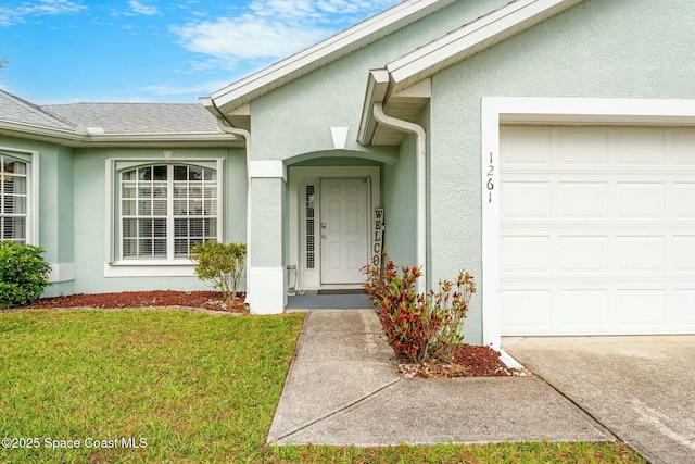 entrance to property featuring stucco siding, a lawn, roof with shingles, and an attached garage