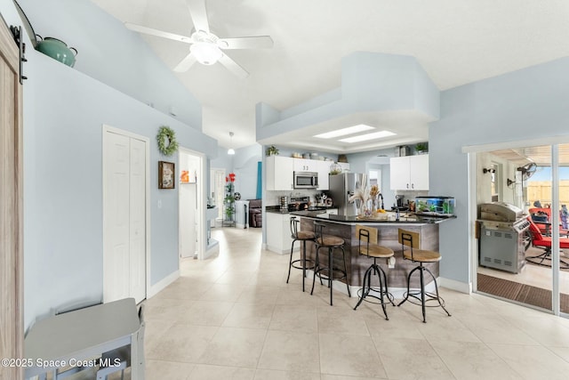 kitchen with a breakfast bar, dark countertops, white cabinetry, a peninsula, and appliances with stainless steel finishes