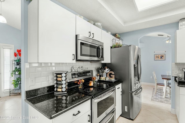 kitchen with light tile patterned floors, stainless steel appliances, arched walkways, and decorative backsplash